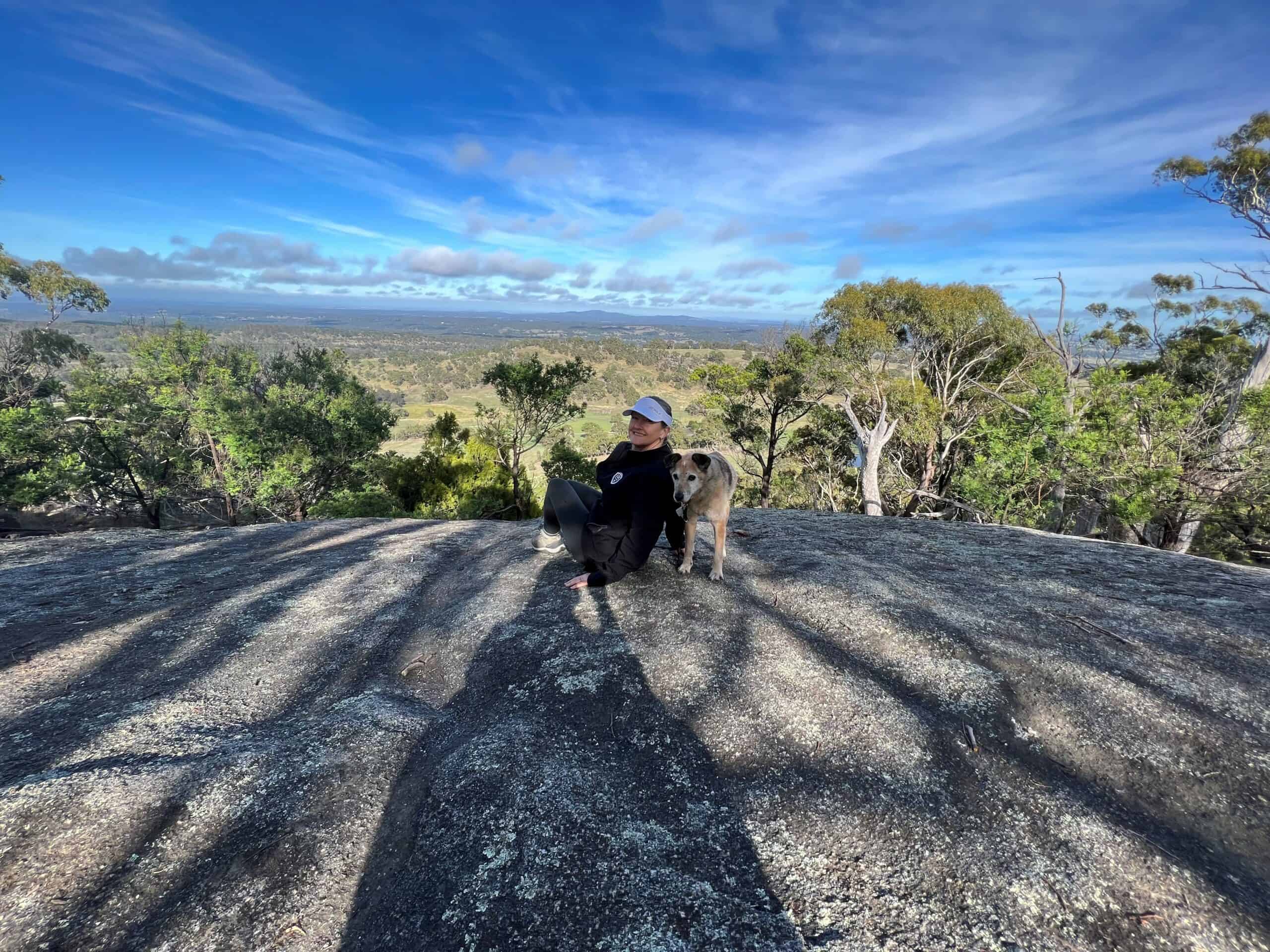 Woman resting on a rocky lookout with her dog during a hike.