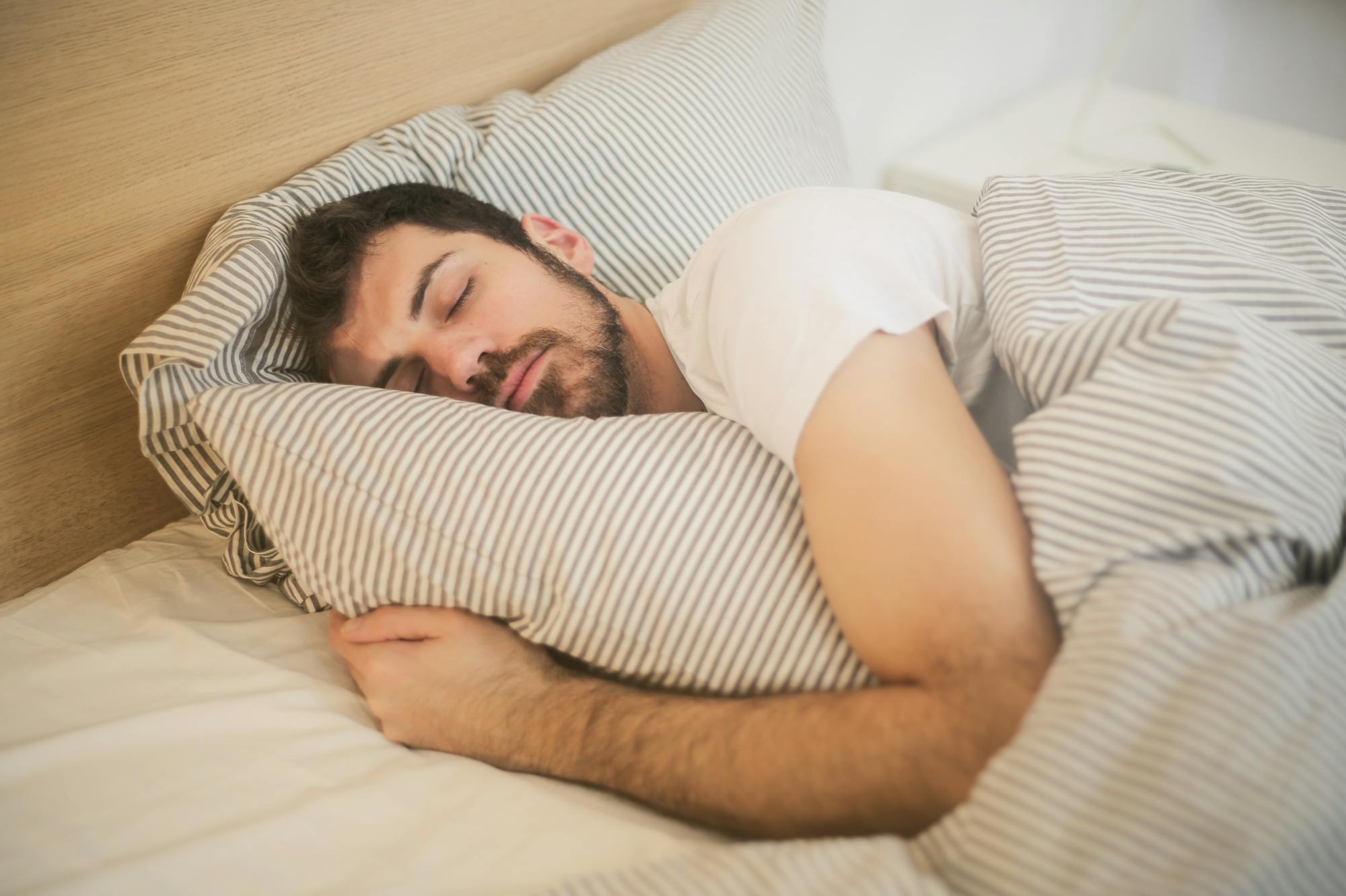 Man sleeping peacefully in bed under striped bedding.