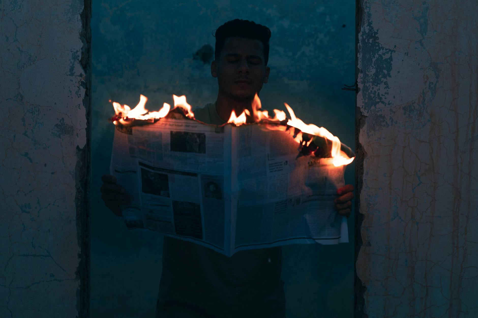 Person holding a burning newspaper in a dark doorway