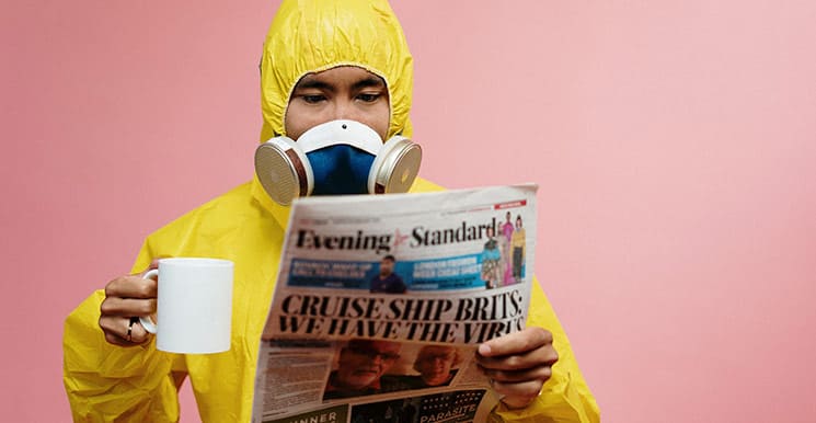 Person in protective suit and mask reading coronavirus news while holding a mug.