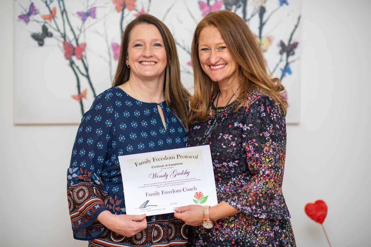 Two women holding a family coaching certificate and smiling indoors.