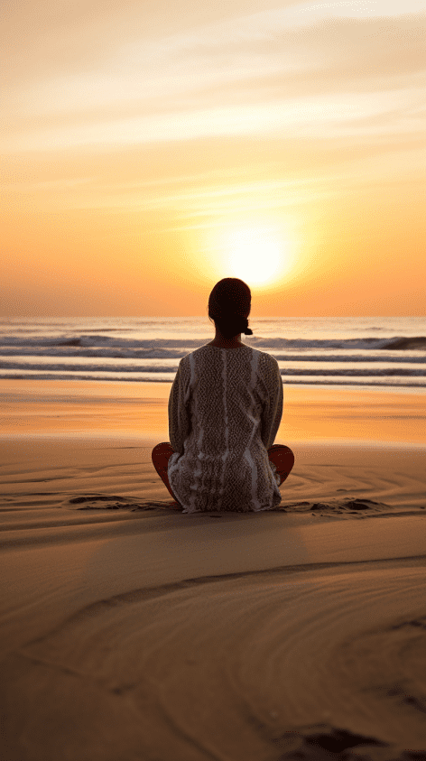 Person sitting on a beach at sunrise in a calm meditative pose.