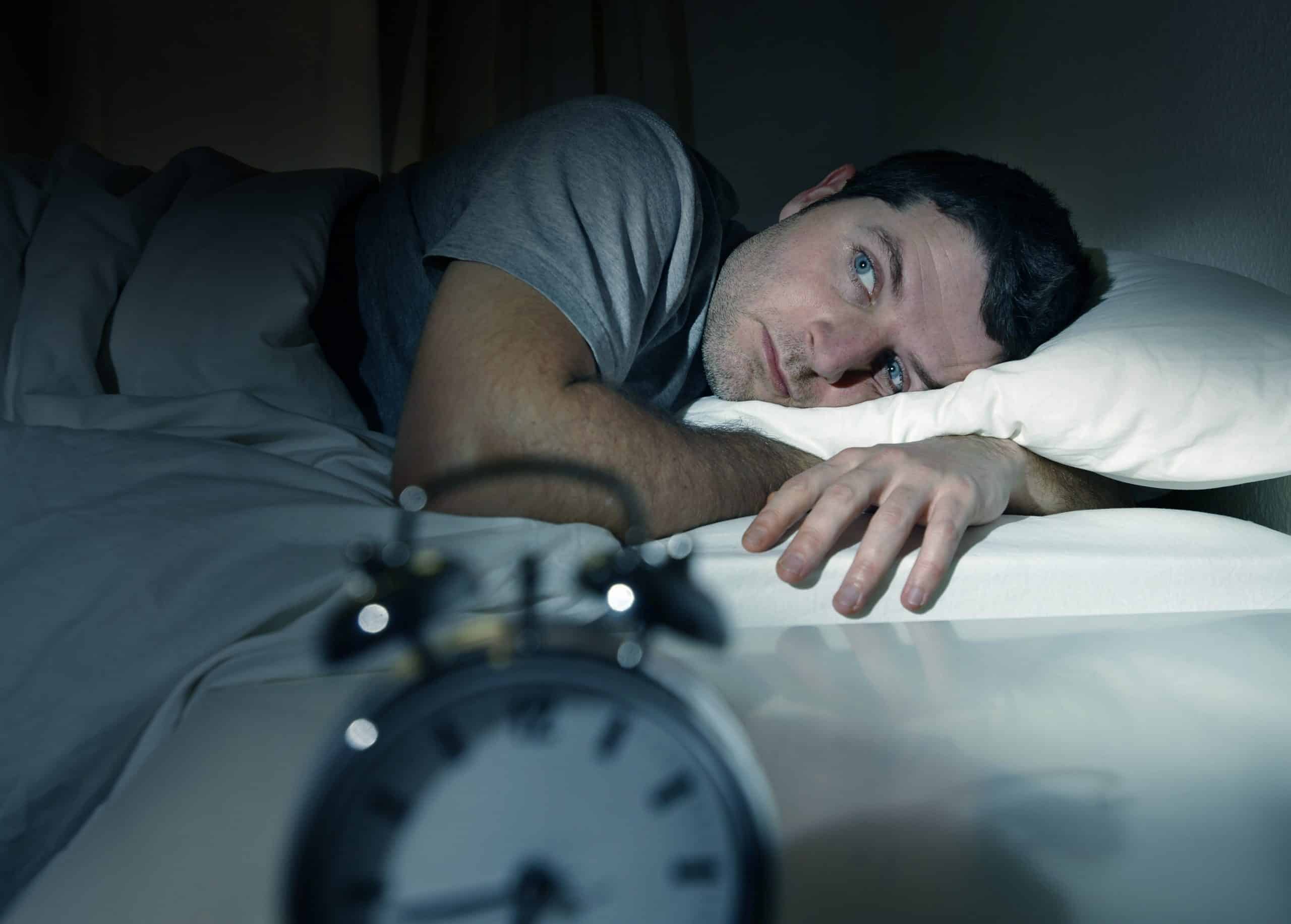 Man lying awake in bed at night with alarm clock in foreground.