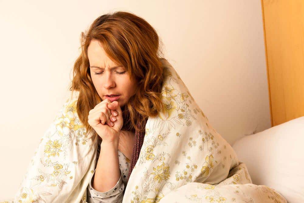 Woman coughing in bed under a blanket