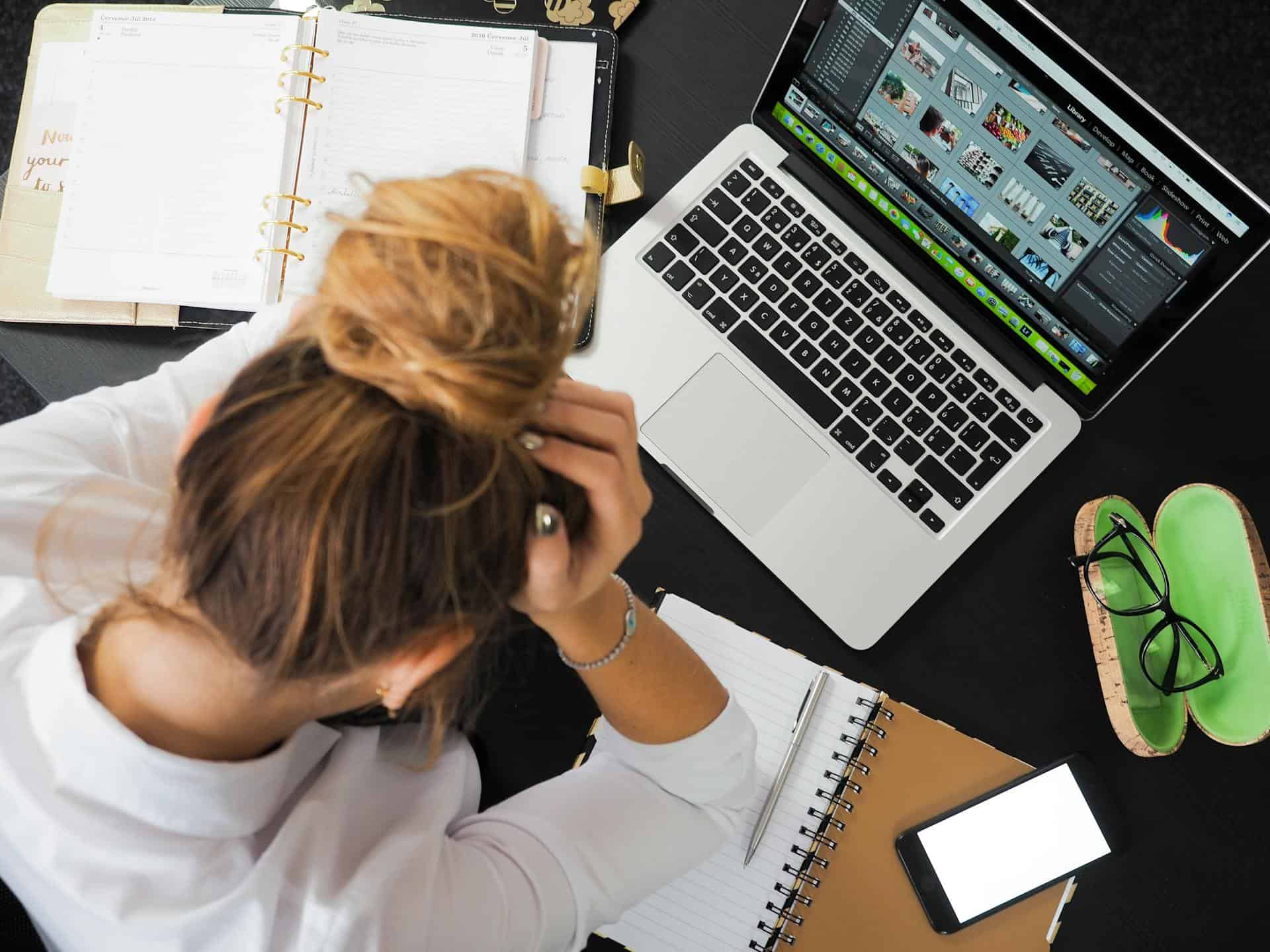 Person at desk holding their head beside a laptop and planner.