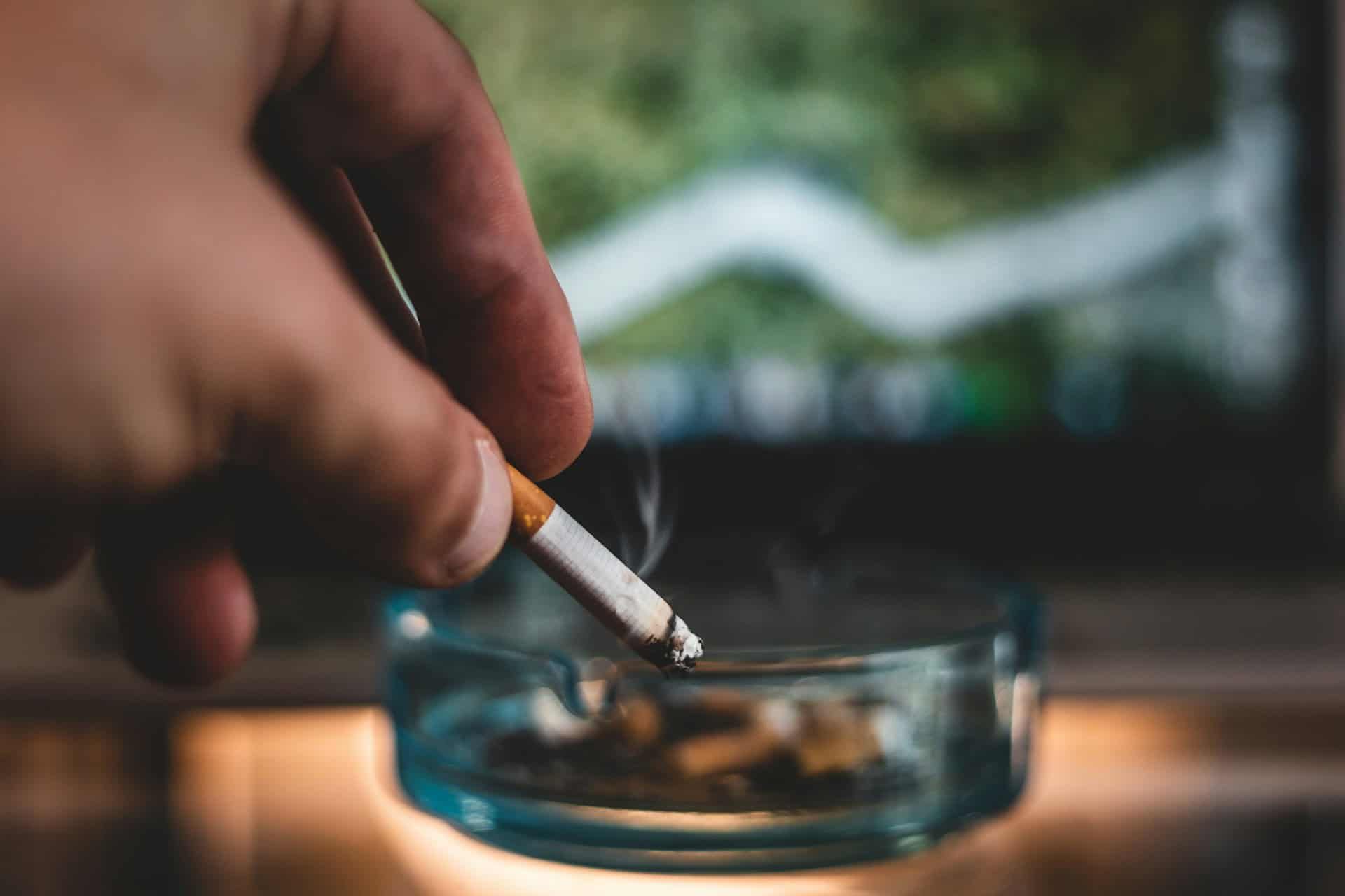 Hand putting out a cigarette in a glass ashtray.