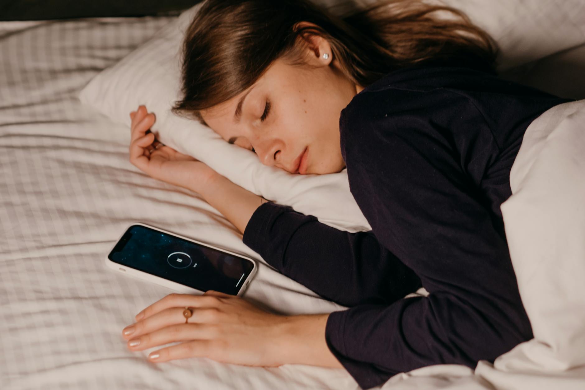 Woman sleeping in bed beside a smartphone.
