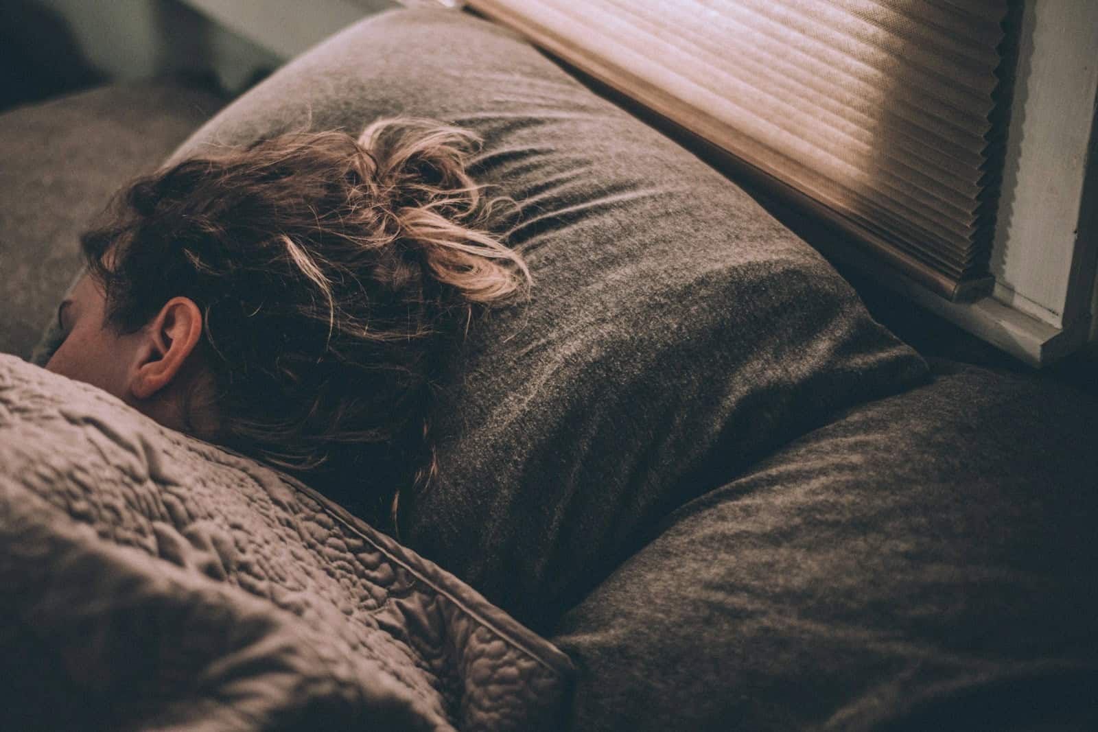 Person sleeping in bed beside a window at night.