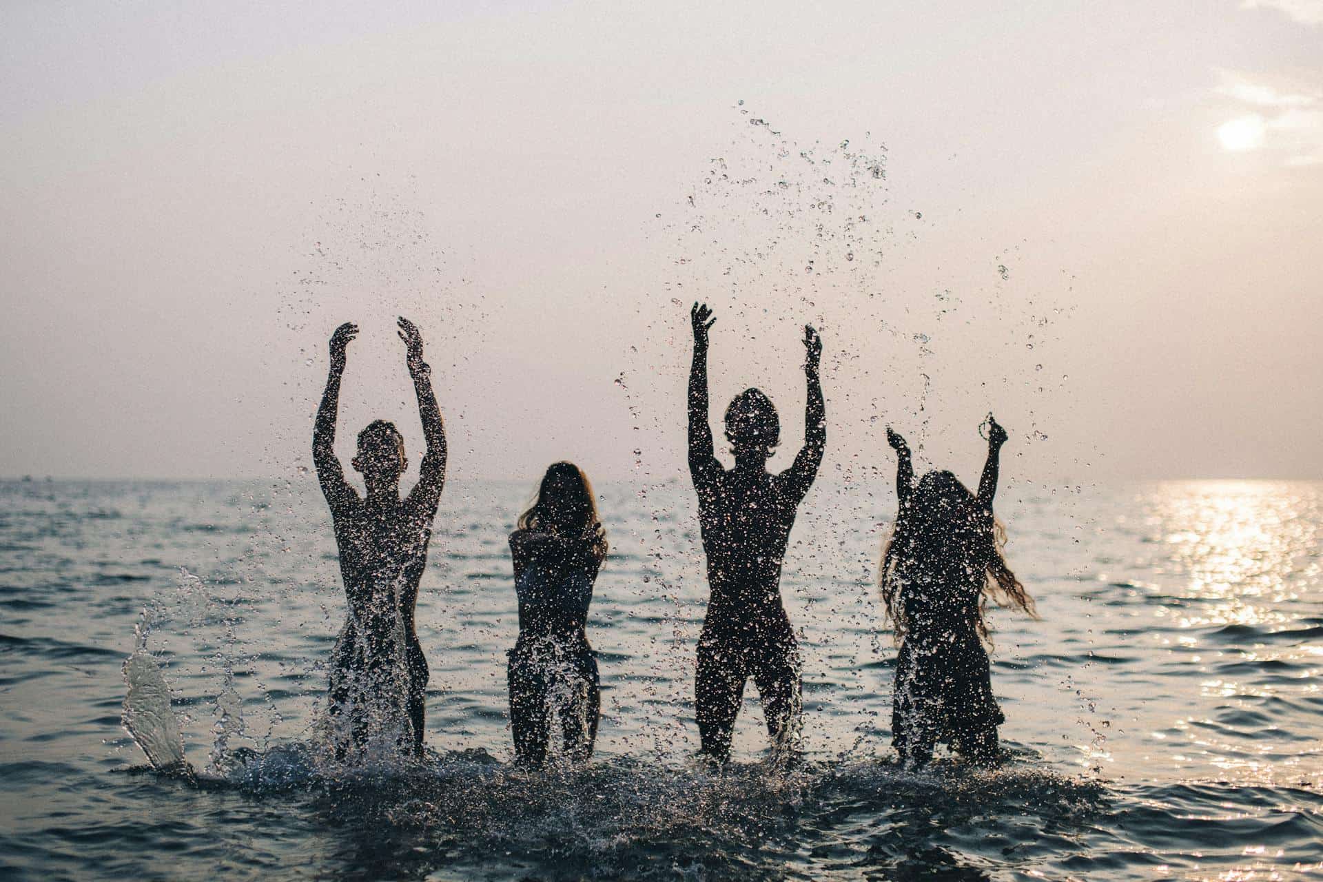 Four people splashing in the sea at sunset.