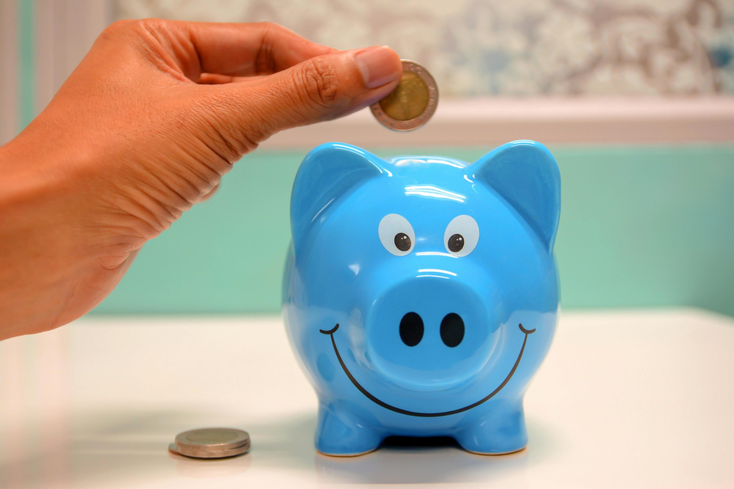 Hand dropping a coin into a blue piggy bank