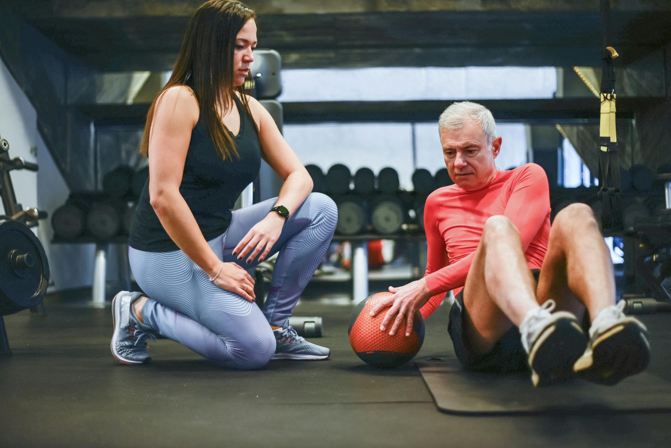 Personal trainer coaching a man through a core exercise in a gym.