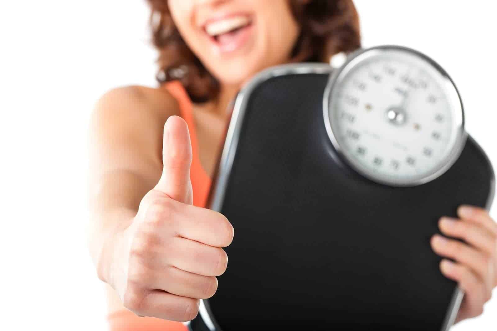 Woman holding a bathroom scale and giving a thumbs up.